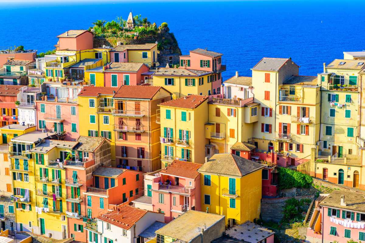 Borgo ligure con case colorate simili a Burano, vista pittoresca tra mare e montagne.